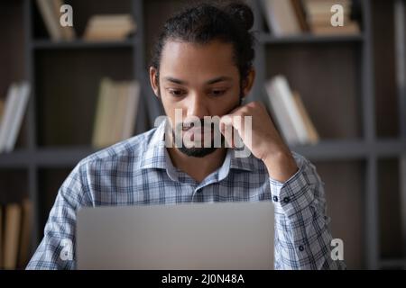 Fokussierter afroamerikanischer Student mit Laptop in der Bibliothek Stockfoto