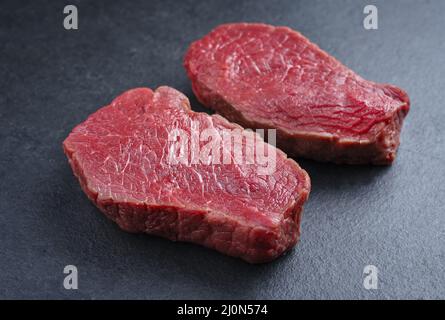 Rohe, trocken gereifte Bison-Beef-Rumpsteaks werden als Nahaufnahme auf schwarzem Hintergrund mit Kopierfläche angeboten Stockfoto