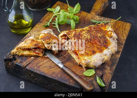 Traditionelle italienische Pizza Calzone mit Thunfisch und Zwiebeln, die als Nahaufnahme auf einem rustikalen alten Holzbrett serviert werden Stockfoto