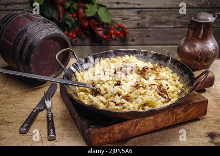 Traditioneller schwäbischer Käsespätzle mit gebratenen Zwiebeln, serviert aus nächster Nähe in einer gusseisernen Bratpfanne auf einer Berghütte Stockfoto