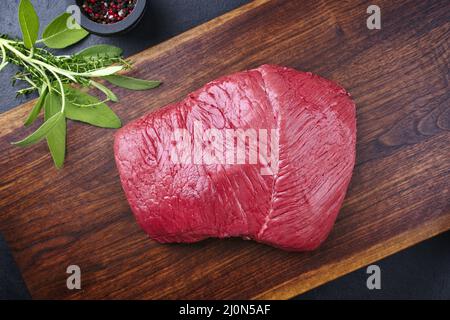 Rohes, trocken gereiftes Bison-Beef-Rumpsteak-Stück als Draufsicht mit Kräutern und Gewürzen auf Holzbrett Stockfoto