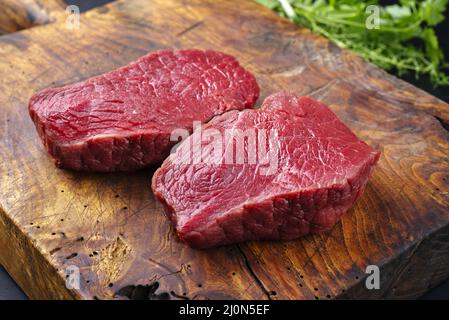 Rohe, trocken gereifte Bison-Beef-Rumpsteaks als Draufsicht mit Kräutern auf einem rustikalen Holzbrett Stockfoto