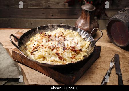 Traditioneller schwäbischer Käsespätzle mit gebratenen Zwiebeln, serviert aus nächster Nähe in einer gusseisernen Bratpfanne auf einer Berghütte Stockfoto