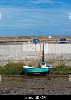 Ein kleines farbenfrohes Fischerboot am Ufer, das auf dem Schlamm bei Low Tide liegt und an einem hellen Tag im Juni an der Hafenmauer von Seahouses festmacht. Stockfoto