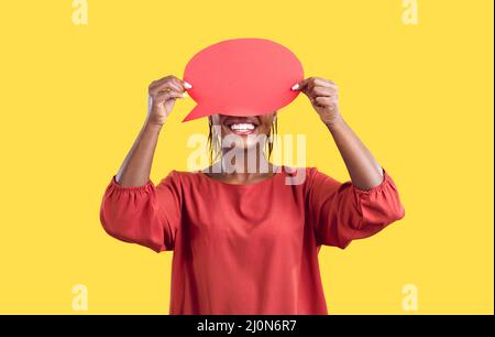 Glückliche junge anonyme schwarze Frau, die ihr Gesicht hinter einer leeren roten Sprechblase versteckt Stockfoto