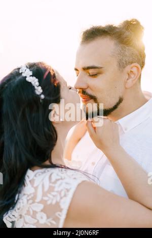 Braut und Bräutigam küssen sich fast gegen den Himmel. Hochformat Stockfoto