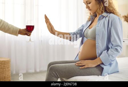 Die Schwangere zeigt eine Stop-Geste vor einem Glas Rotwein, als sie den Alkohol aufgibt. Stockfoto