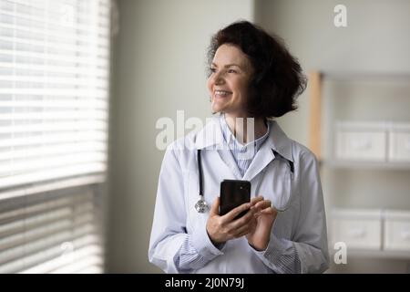 Erfolgreiche glückliche leitende Ärztin mit App auf dem Smartphone Stockfoto