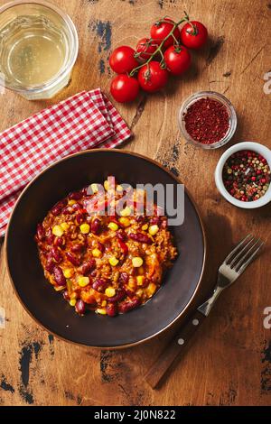 Chili Con Carne mit Hackfleisch, Bohnen und Mais in dunkler Schüssel auf Holzboden. Mexikanische und texanische Küche Stockfoto