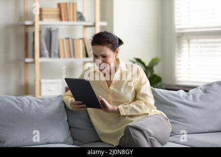 Positiv fokussierte reife freiberufliche Frau mit Tablet-Computer zu Hause Stockfoto