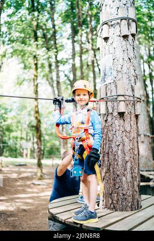 Boy in einem Helm mit Sicherheitsausrüstung steht auf einer hölzernen Plattform Stockfoto