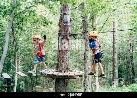 Der Junge geht am Kabel entlang zur Holzplattform und der zweite geht entlang der Agility-Brücke Stockfoto