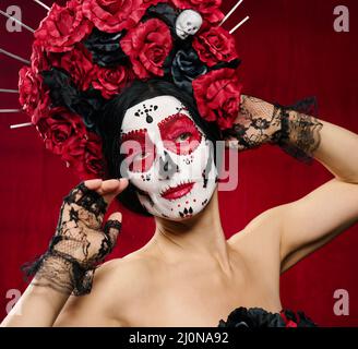Porträt einer schönen Frau mit einem Zuckerschädel Make-up mit einem Blumenkranz auf dem Kopf, roter Hintergrund Stockfoto