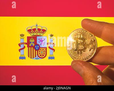 Mit einem physischen goldenen Bitcoin über der spanischen Flagge. Spanien als Investor in Kryptowährung und Blockchain-Technologie. Finanzieller Hintergrund Stockfoto