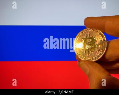 Mit einem physischen goldenen Bitcoin über der russischen Flagge. Russland als Investor in Kryptowährung und Blockchain-Technologie. Finanzieller Hintergrund Stockfoto