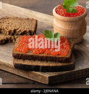 Kaviar aus rotem Lachs liegt auf einem Stück Roggenbrot. Brauner Holztisch Stockfoto