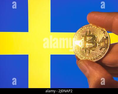 Mit einem physischen goldenen Bitcoin über der schwedischen Flagge. Schweden als Investor für Kryptowährung und Blockchain-Technologie. Finanzieller Hintergrund Stockfoto