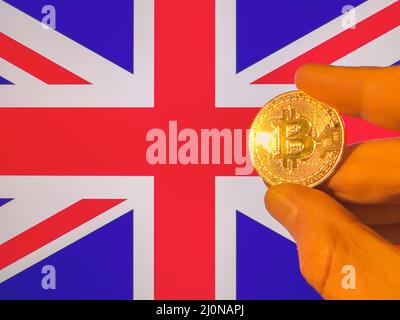 Mit einem physischen goldenen Bitcoin über der britischen Flagge. England als Investor in Kryptowährung und Blockchain-Technologie. Finanzieller Hintergrund Stockfoto