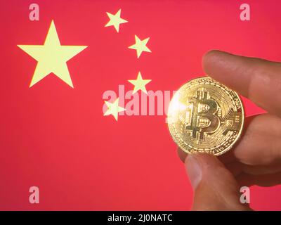 Mit einem physischen goldenen Bitcoin über der chinesischen Flagge. China als Investor für Kryptowährung und Blockchain-Technologie. Finanzieller Hintergrund Stockfoto