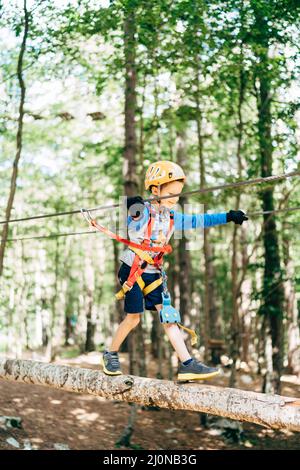 Junge im Helm geht auf dem hölzernen Luftweg im Abenteuerpark Stockfoto