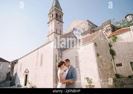 Der Bräutigam umarmt die Braut auf dem Steinplatz vor der Kirche Stockfoto