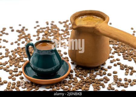 Türkischer Kaffee auf weißem Hintergrund. Rustikale Tasse und irdenen Kaffeekocher. Verstreute Kaffeebohnen auf dem Boden Stockfoto