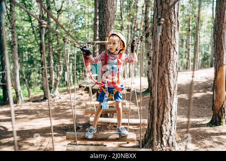 Boy steht auf der Agility Bridge und hält sich an den Seilgeländern fest Stockfoto