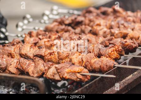 Schweinefleisch Spieß, gegrillt oder gebraten in einem Grill auf einem offenen Feuer und Flammen, Schaschlik oder Schaschlyk für ein Picknick mit Mistgabeln, aus der Nähe Stockfoto