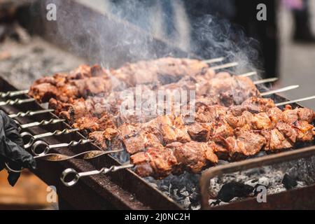 Schweinefleisch Spieß, gegrillt oder gebraten in einem Grill auf einem offenen Feuer und Flammen, Schaschlik oder Schaschlyk für ein Picknick mit Mistgabeln, aus der Nähe Stockfoto