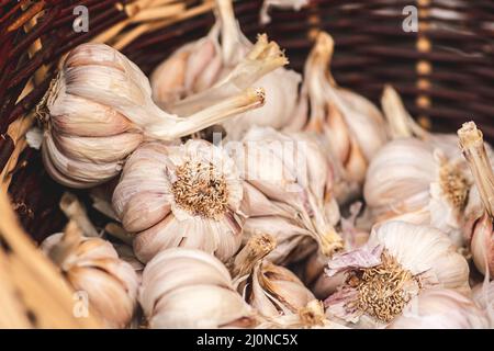 Eine Gruppe von Knoblauchzwiebeln und Nelken in einem Korbkorb unter der Sonne auf einem regionalen Lebensmittelmarkt auf der Straße, aus der Nähe Stockfoto