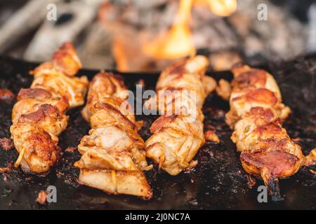 Vorbereiten von Hähnchenfleischspießen, gegrillt oder gebraten in einem Grill auf einem offenen Feuer und Flammen, Schaschlik oder Schaschlik für ein Picknick mit Mistgabeln, schließen Stockfoto