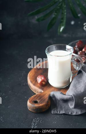 Ramadan Kareem Essen und Getränke. Teller mit Datteln, Glas Milch und Dattelpalmzweig auf schwarzem Hintergrund. Gerechter Muslimischer Lebensstil. Vegetarische Gerichte. S Stockfoto