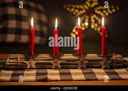 Advent Holzstäbchen Kerzenhalter mit silbernen Sternen mit den Nummern 1,2,3,4. Vier brennende rote Kerzen. Weihnachtsdekoration. Stockfoto