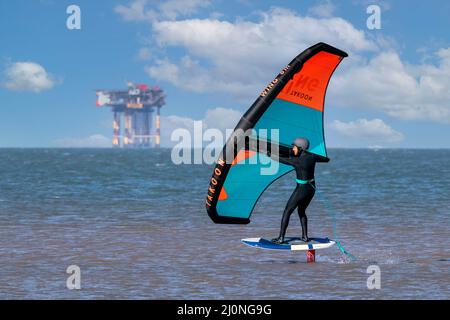 Southport, Merseyside, Großbritannien. 20.. März 2022. Ein Wing Surfer geht mit seinem Foil X-Glide und Takoon Wing am Strand von Southport in Merseyside ans Meer. Wingsurfing ist einfach die Verwendung eines Handflügels, um ein Brett auf dem Wasser zu treiben. Die Verwendung von Flügeln auf Surfbrettern und Windsurfbrettern gibt es seit Mitte der 1980er Jahre. Quelle: Cernan Elias/Alamy Live News Stockfoto