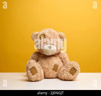 Niedlicher brauner Teddybär mit Aufnäher sitzt auf einem gelben Hintergrund, Kinderspielzeug Stockfoto