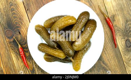 Hausgemachte Salzgurken mit Chilli auf dem Teller auf Holzboden. Häusliche Erhaltung. Selektiver Fokus. Blick von oben, Essen von oben. Nahaufnahme. Stockfoto