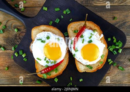 Gebratenes Ei-Sandwich mit Eigelb, Chili auf gerösteter Brotscheibe, die mit grünen Zwiebeln bestreut ist. Selektiver Fokus. Draufsicht. Nahaufnahme. Stockfoto