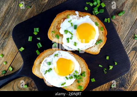 Gebratenes Ei-Sandwich mit Eigelb, Chili auf gerösteter Brotscheibe, die mit grünen Zwiebeln bestreut ist. Selektiver Fokus. Draufsicht. Nahaufnahme. Stockfoto