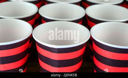 Rote und schwarze Einweg-Becher aus umweltfreundlichem Papier für Kaffee oder heiße Getränke vor dunklem Hintergrund. Selektiver Fokus. Nahaufnahme. Stockfoto