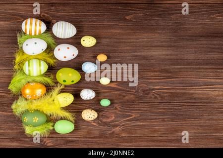 Happy Easter Konzept. Bunte Ostereier mit hellen Federn auf dunklem Holzhintergrund. Blick von oben. Platz für Beschriftung, Text. Basis für ein Stockfoto