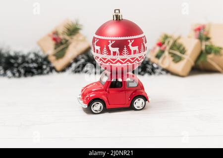 Spielzeugauto mit roter weihnachtskugel in der Nähe von Geschenkboxen. Hohe Qualität und Auflösung schönes Fotokonzept Stockfoto