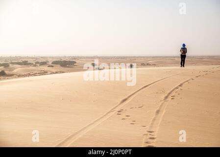 Eine Touristenfrau, die auf einer Sanddünenlandschaft in der Wüste des Adrar-Plateaus, Mauretanien, unterwegs ist Stockfoto