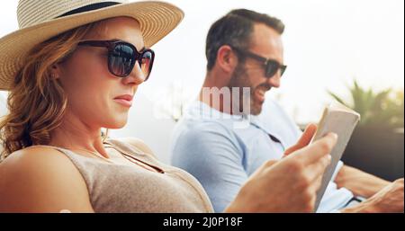 Ein genauerer Blick auf das Menü. Aufnahme eines reifen Paares, das auf Liegestühlen nebeneinander sitzt und im Urlaub im Freien liest. Stockfoto