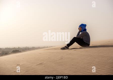 Eine Touristenfrau, die an einem windigen Tag auf einer Sanddüne in der Wüste Adrar-Plateau in Mauretanien sitzt Stockfoto