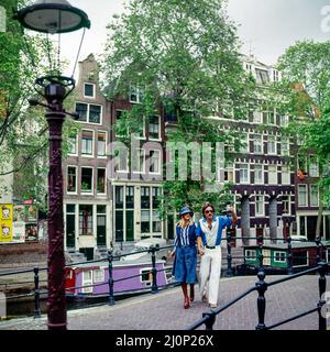 Vintage Amsterdam 1970s, stilvolles junges Paar, das auf der Kanalbrücke spazieren geht, Lastkähne, Häuser, Holland, Niederlande, Europa, Stockfoto