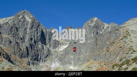 Eine rote Seilbahn auf dem Weg von Skalnate pleso zum Lomnitzer Gipfel. Die rote Gondel fährt auf den Lomnica-Gipfel in der Hohen Tatra. Stockfoto