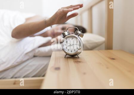 Frau, die den Wecker abgestellt hat, während sie im Bett lag. Hohe Qualität und Auflösung schönes Fotokonzept Stockfoto