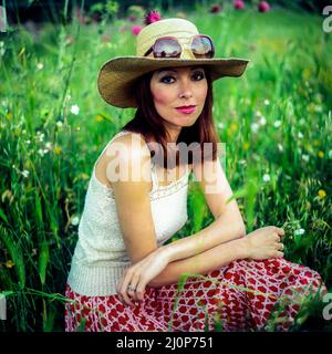 Vintage Italy 1970s, hübsches Frauenporträt mit Sonnenbrille auf Strohhut auf Wiese, Europa, Stockfoto