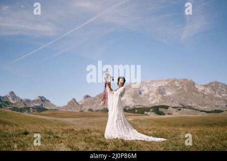 Braut mit einem Tamburin mit Blumen geschmückt steht auf einem Feld vor einem Hintergrund von Bergen Stockfoto