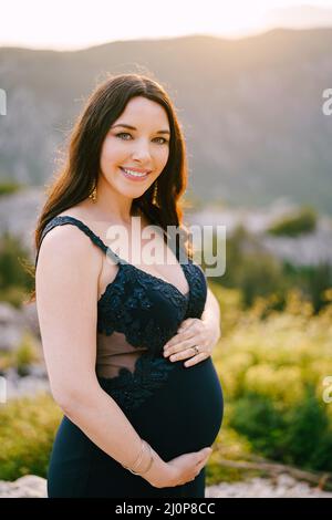 Eine Schwangere, die ihren Bauch umarmt, steht auf einem felsigen Berg Stockfoto